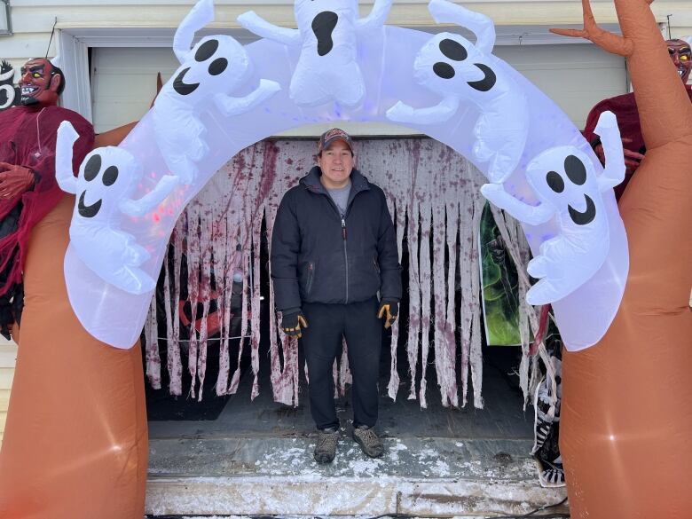 A man stands under an inflatable archway of ghosts, with other Halloween decorations around him.