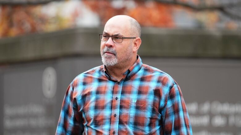 A man in a patterned shirt walks outside in the autumn.