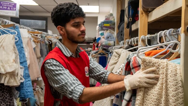 A person wearing a red apron and white gloves sifts through clothing on a rack.