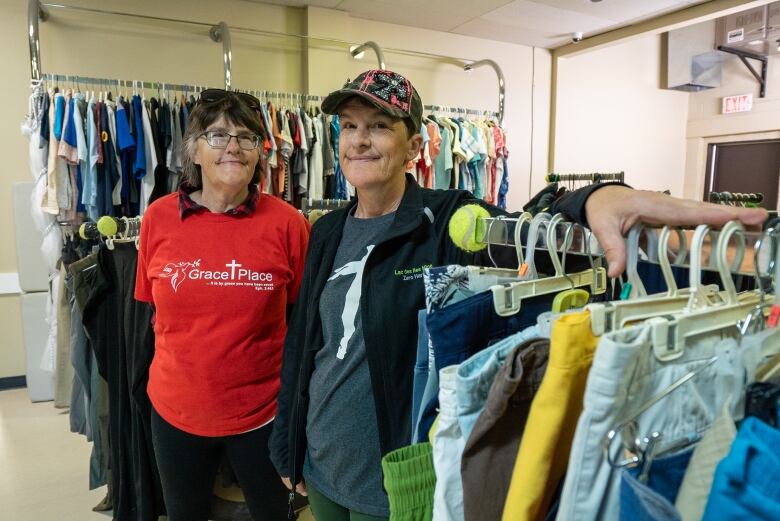 Two people stand together amid clothing racks.