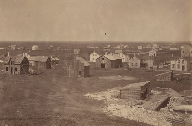 A monochromatic photo shows wooden houses spread out over a wide area. There are no paved streets.