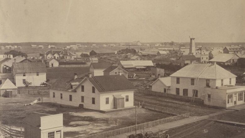 A monochromatic photo shows wooden houses spread out over a wide area. There are no paved streets.