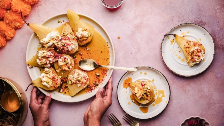 Overhead shot of a white serving plate with poached pears on it sitting on a purple table. 2 smaller plates with a pear on each sit on the left. 