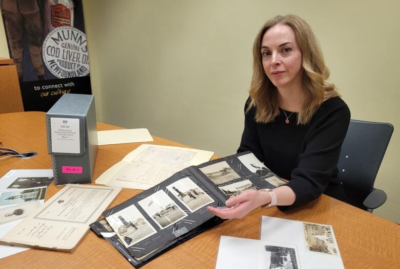 A woman sits at a table, displaying photo albums full of old pictures.