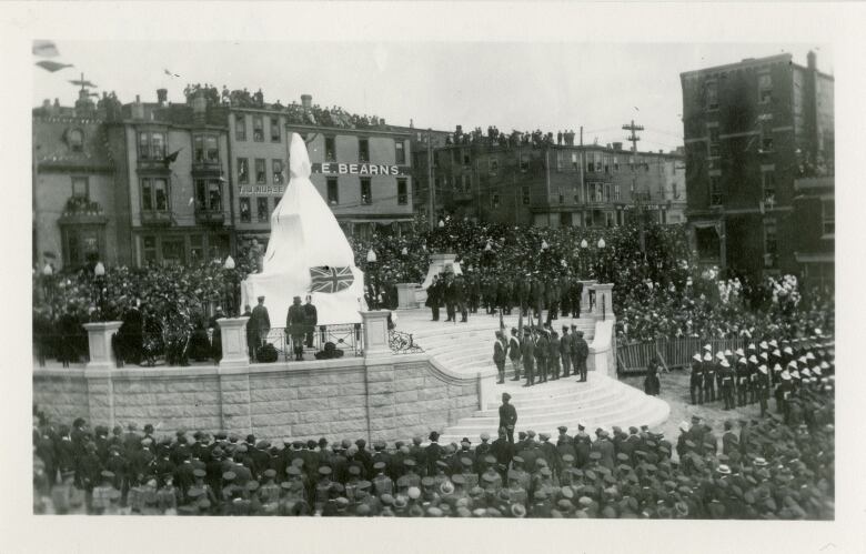 An old black and white image of a crowd of people waiting for a statue to be unveiled. 