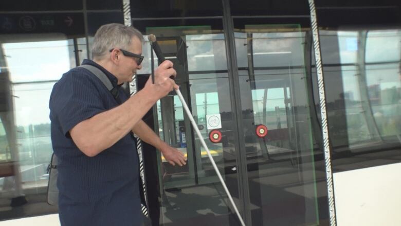 A man holding a cane is using his hand to search for a button.