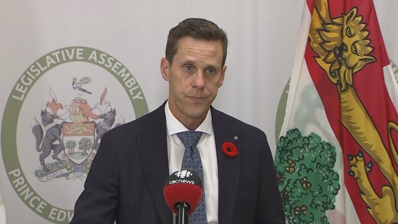 A man in a dark suit, white shirt and blue tie standing before a backdrop that says P.E.I. legislative assembly.