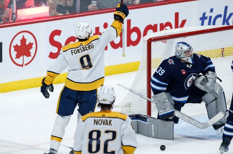 A hockey player in yellow and white raises his arm after scoring