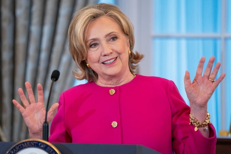 A woman stands in front of a microphone and gestures with her hands.