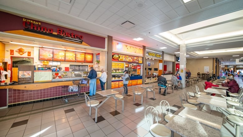 A small shopping centre food court with a few people lined up for food and at the tables.