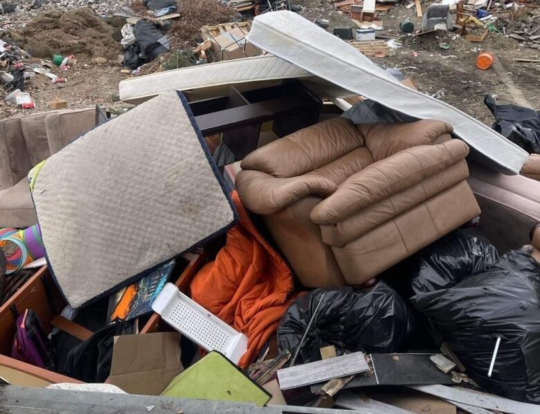 A brown chair sits tilted on a pile of garbage at the dump.