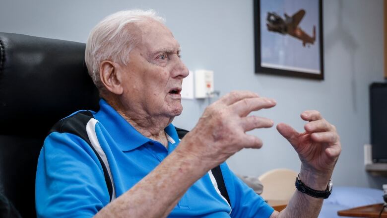 A older man sits and speaks. Over his left shoulder, is a portrait of Second World War bomber aircraft.