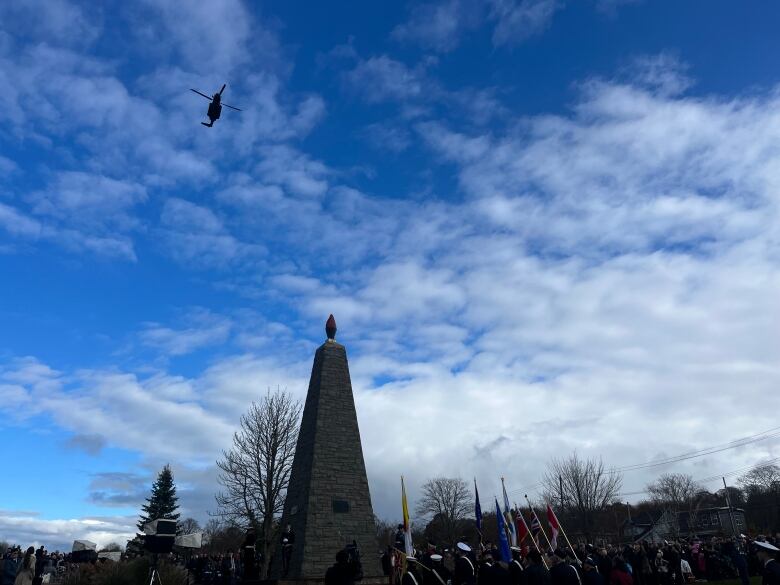 A helicopter, and cenotaph are shadows in front of a blue sky. 