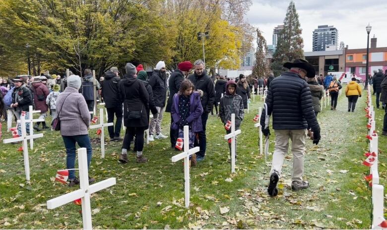 People of all ages walk between white crosses adorned with small Canada flags.