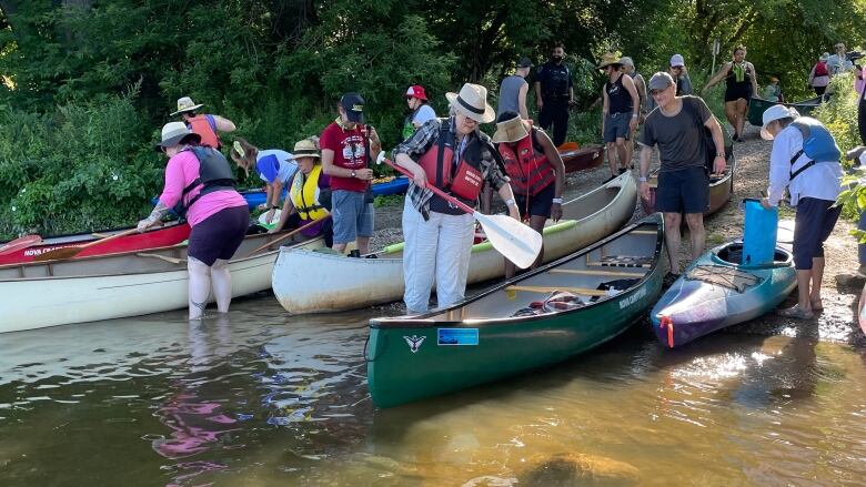 People stand in shallow water surrounded by canoes. 