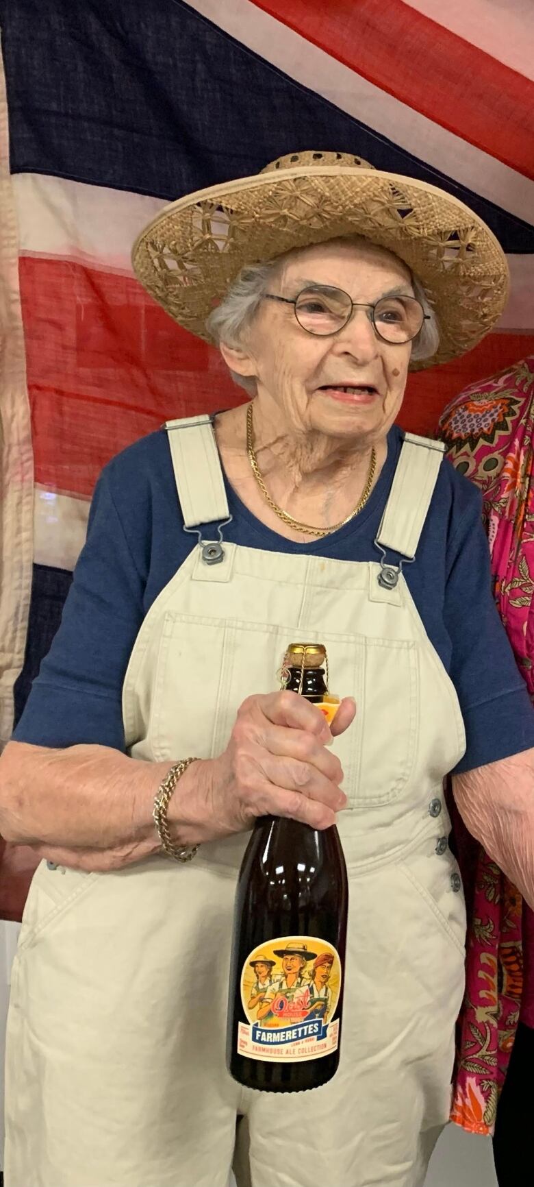 98 year old Jean Brett poses for a photo in a straw hat and overalls. She was a former Farmerette.