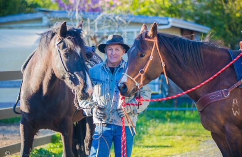 A man wearing a cowboy hat holds two brown horses.