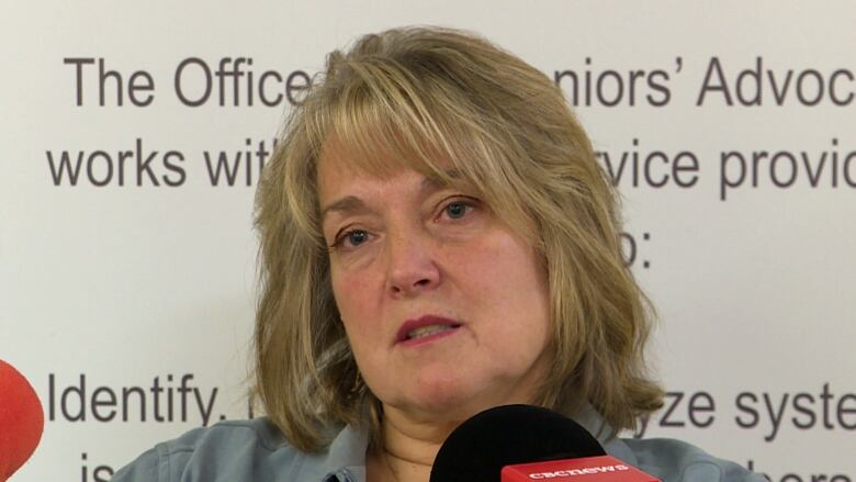 A woman with blond hair sits in front of microphones.