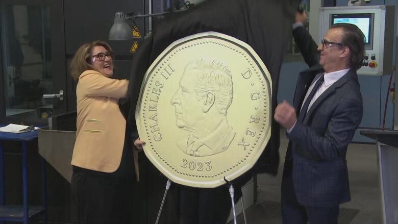 Three people remove a cover from a large replica coin.