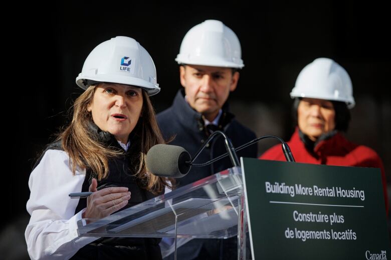 A woman speaks at a podium, in front of two onlookers.