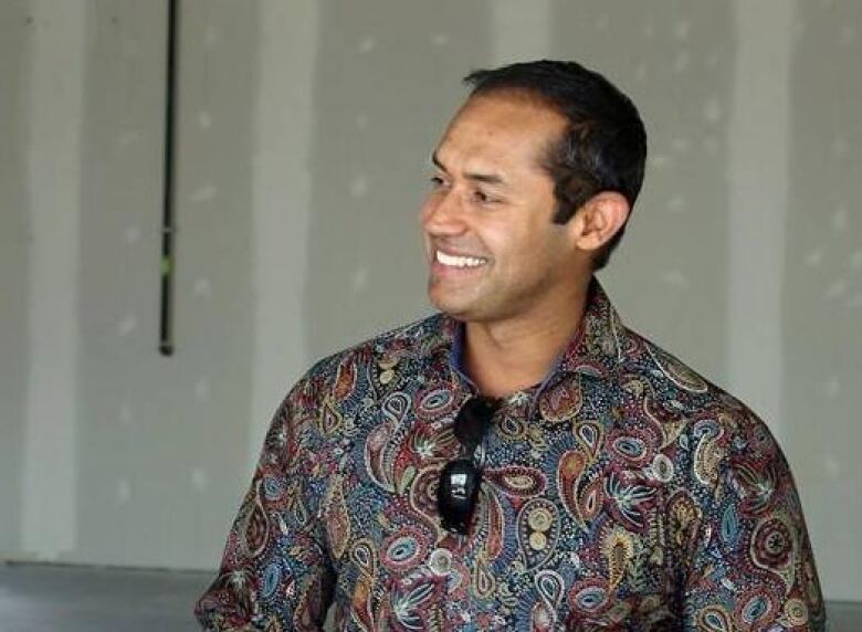 A smiling man in a colourful patterned shirt.