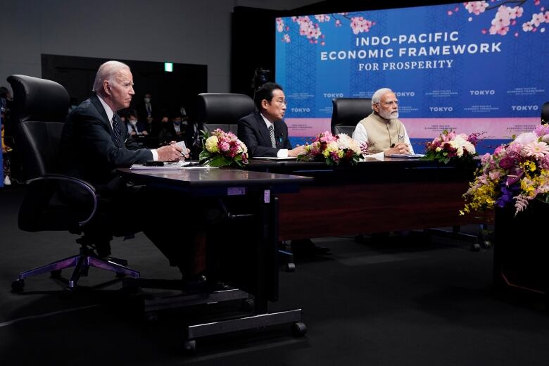 Three men sit around a boardroom table.