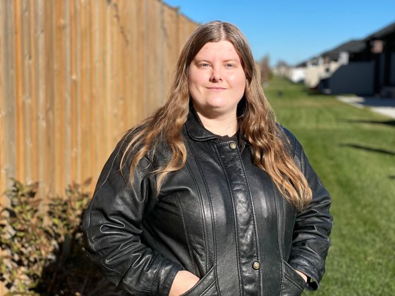 A woman in a leather jacket stands outside 