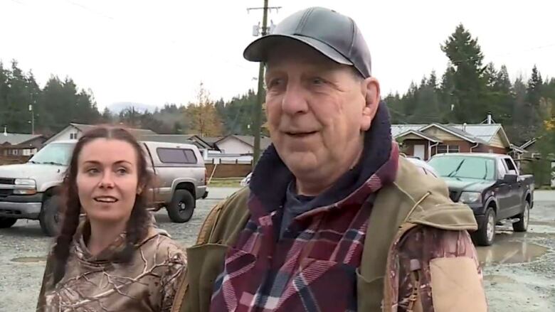 A man wearing a baseball hat looks relieved next to a woman wearing a brown hoodie.