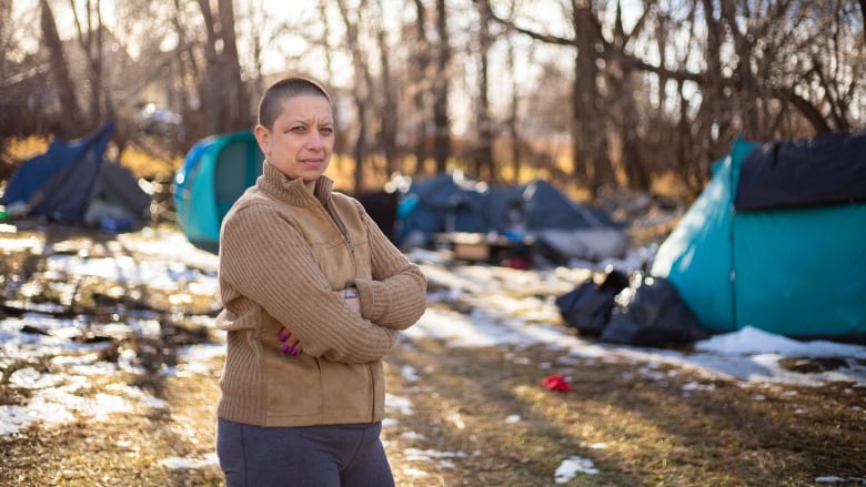 A woman stands in a unhoused encampment.