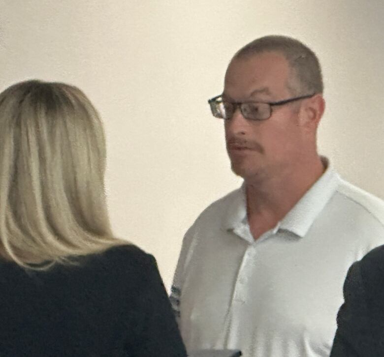 A man wearing a white shirt is shown speaking with a woman.