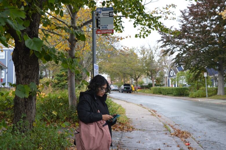 A woman waits at bus stop on leafy street