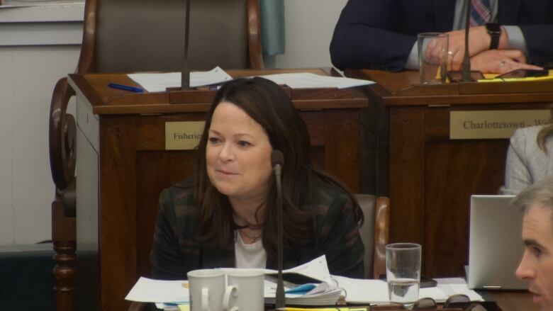 A woman in a plaid jacket and white shirt sits while posing questions about the sick leave bill.