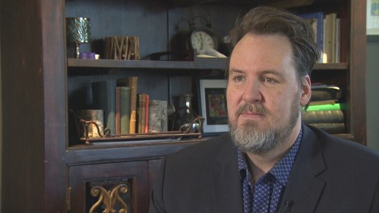 A man with a beard speaks to a reporter off camera.