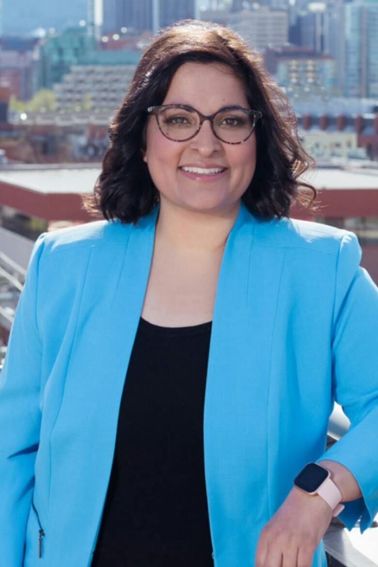 A woman leans against a balcony railing with the city of Calgary behind her.