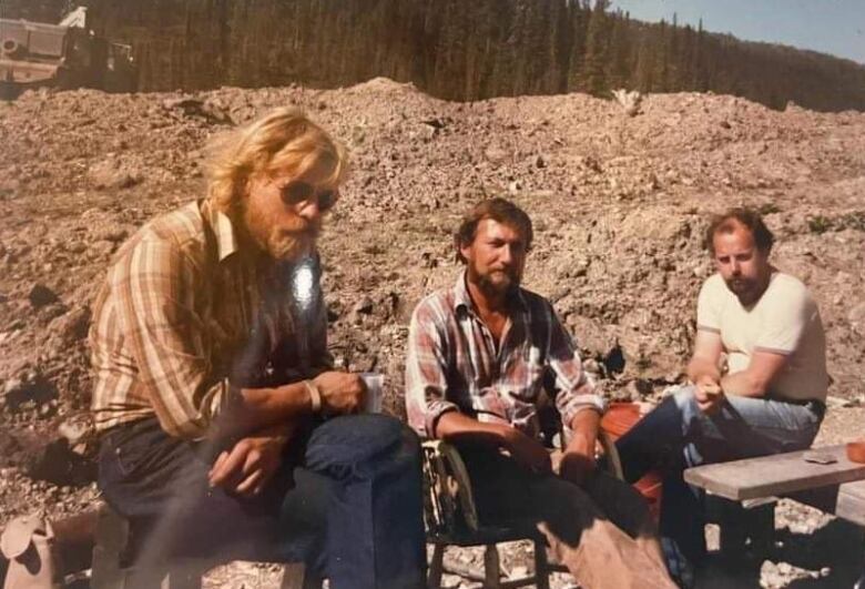 Three men sit outside at a mine site in an old photo.