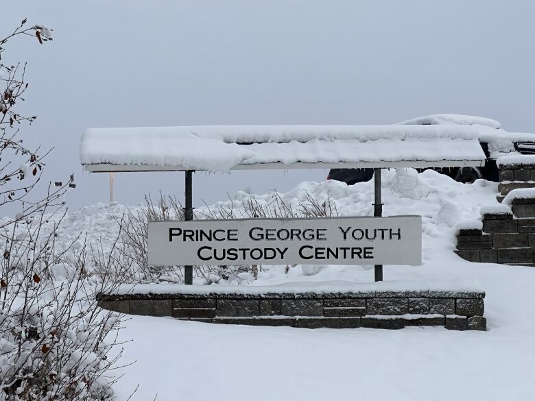 A white wooden sign is seen embedded in a snow drift. In black capital letters it says Prince George Youth Custody Centre.