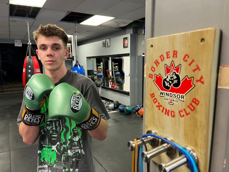 Jayden poses with his green gloves on standing next to a sign that says Border City Boxing Club