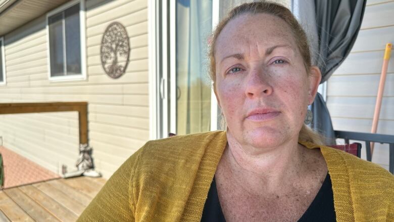 A woman sits outside on a patio looking straight at the camera.