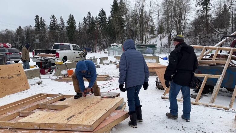 A group of people works on a wooden structure outdoors in the snow.