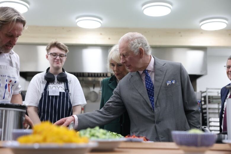 A person points toward a plate of food sitting on a counter as other people look on.