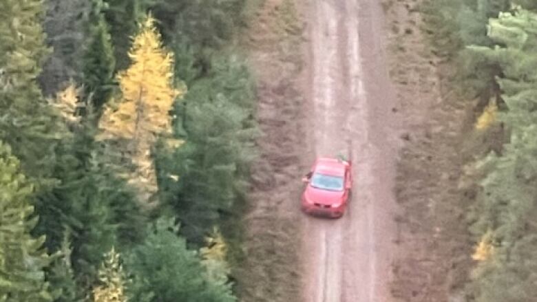 a red sedan in the woods on a muddy trail 