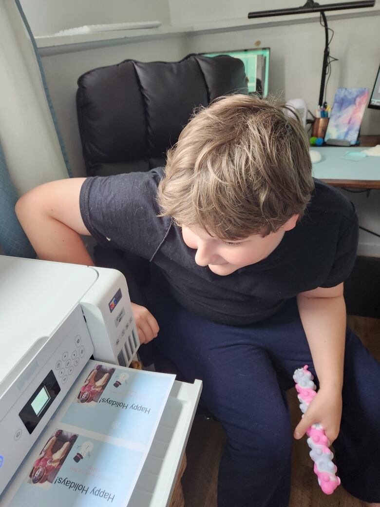 A young boy waits patiently next to a printer as holiday cards are printed out.