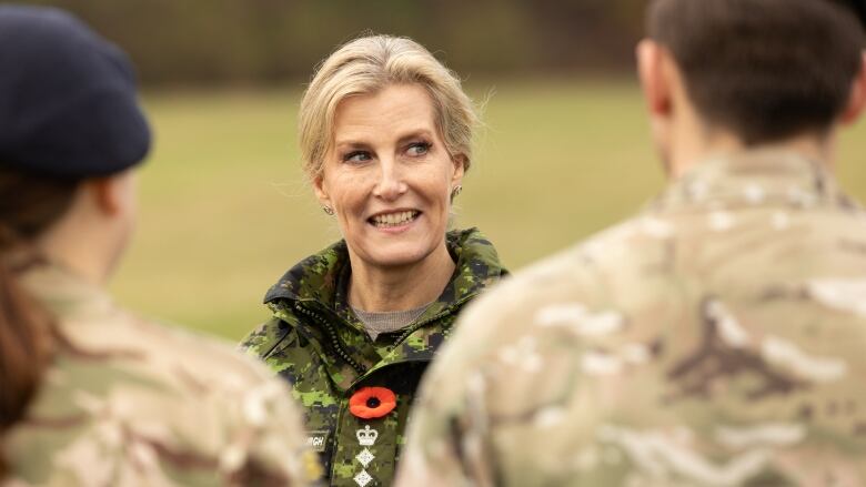 A person in military fatigues talks to two others in soldier's uniforms.