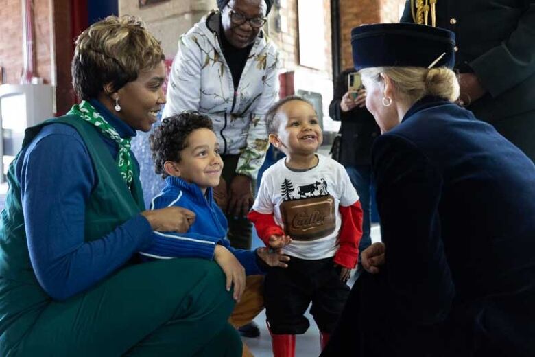 An adult kneels down to speak with children.