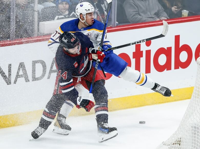 A hockey player in a white jersey collides with a hockey player in a dark blue jersey.