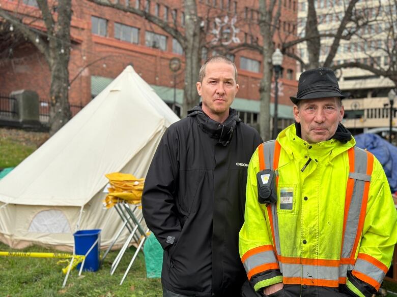 Two men in rain jackets stand in front of a yurt-style tent.