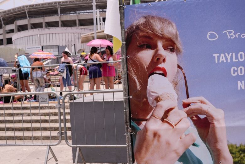 People in the background hold umbrellas to shield themselves from the heat and sun. A poster of a woman licking a cone of ice cream is in the foreground.