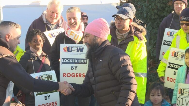 A man shakes hands with another man with workers holding picket signs in the back. 