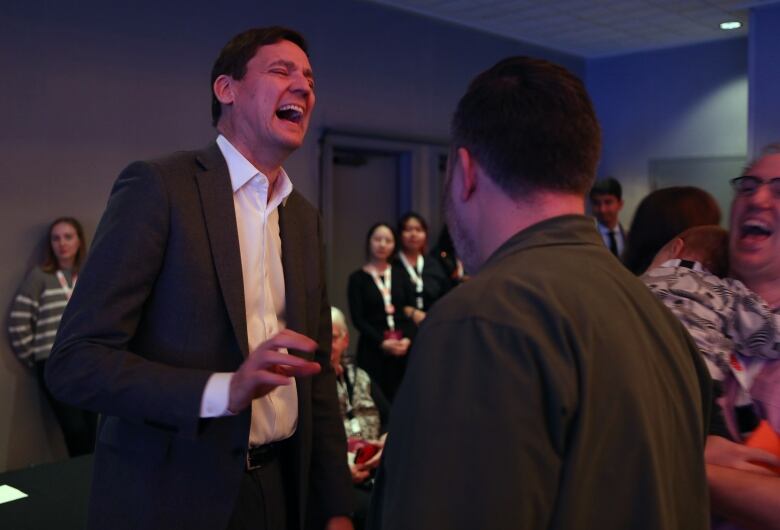 A tall white man laughs broadly at an event.