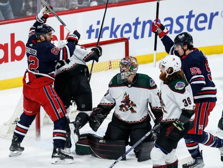 Hockey players cluster around a net guarded by a goaltender.